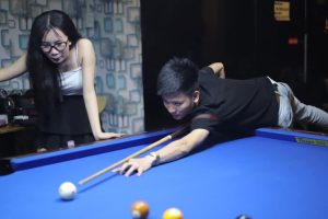 a man lying on the pool table with a woman looking at the ball